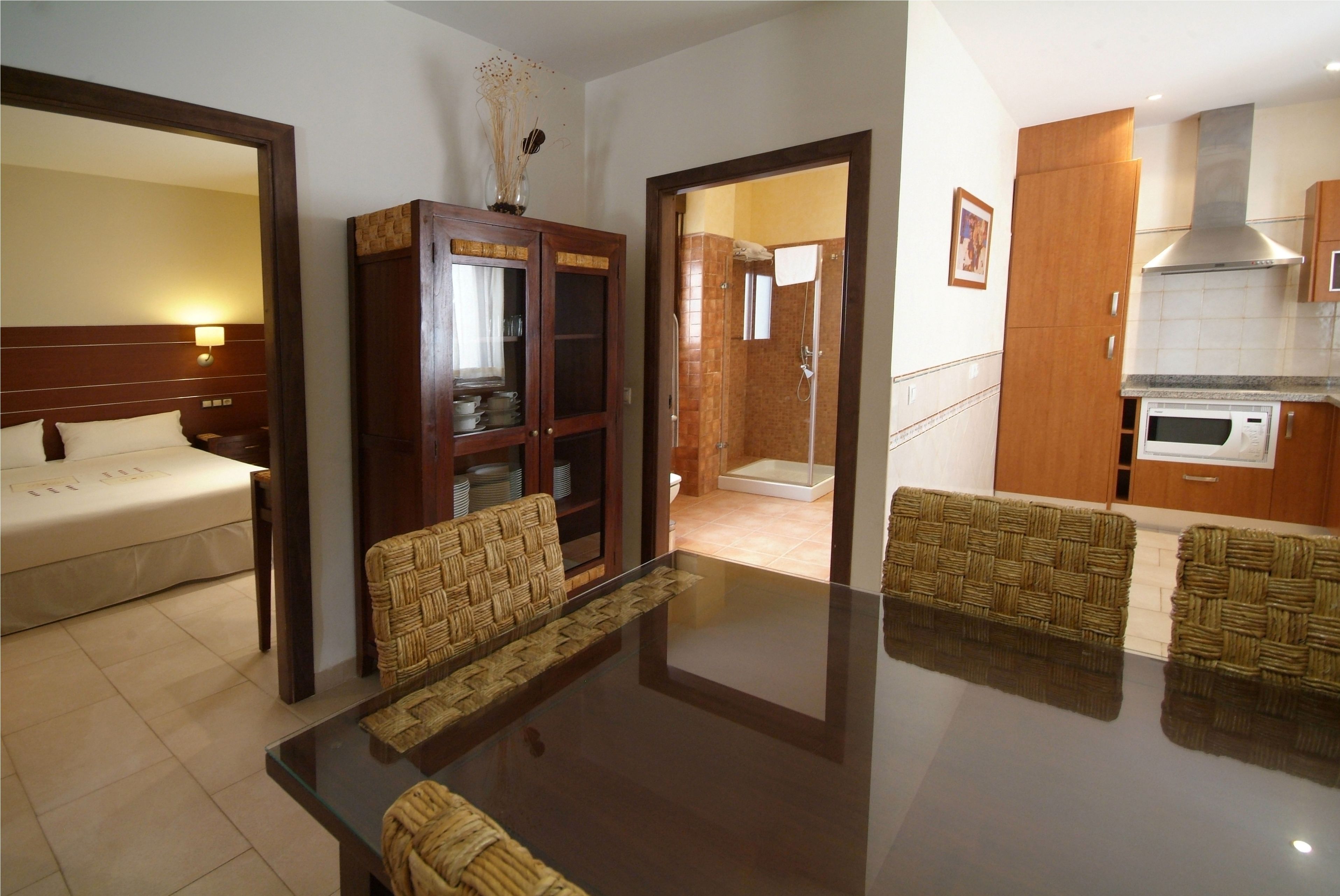 Quarto de hotel com cama, mesa de jantar com cadeiras, armário de madeira e cozinha equipada com micro-ondas.