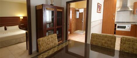 Quarto de hotel com cama, mesa de jantar com cadeiras, armário de madeira e cozinha equipada com micro-ondas.