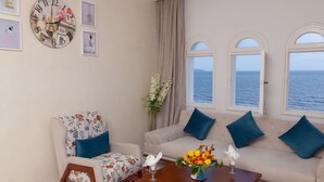 A room with a sofa, armchair, and a table with a vase of flowers. There is a clock on the wall and a window with a view of the sea. - Hotel Ezzahra Dar Tunis (Ezzahra)