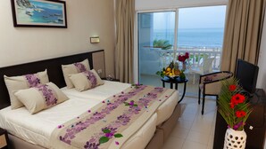A hotel room with a bed, a desk, a chair, a vase with flowers, and a balcony with a view of the sea. - Hotel Ezzahra Dar Tunis (Ezzahra)