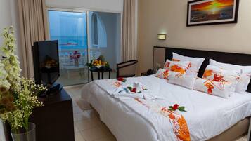 Habitación de hotel con cama, televisor, escritorio y vista al océano a través de un ventanal.