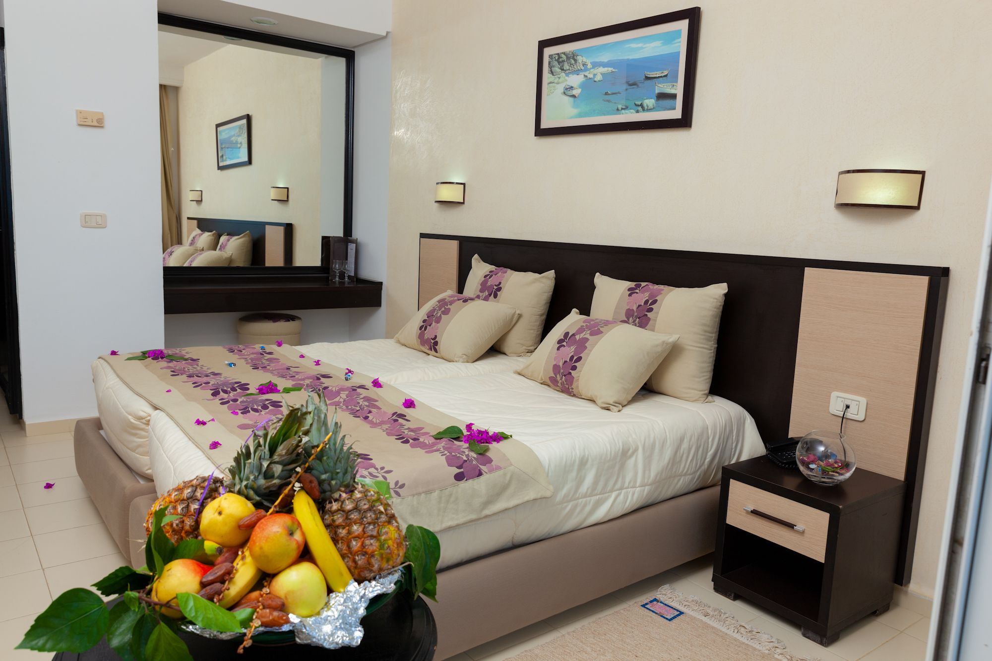 Habitación de hotel con cama, mesita de noche, espejo e imagen colgada en la pared.