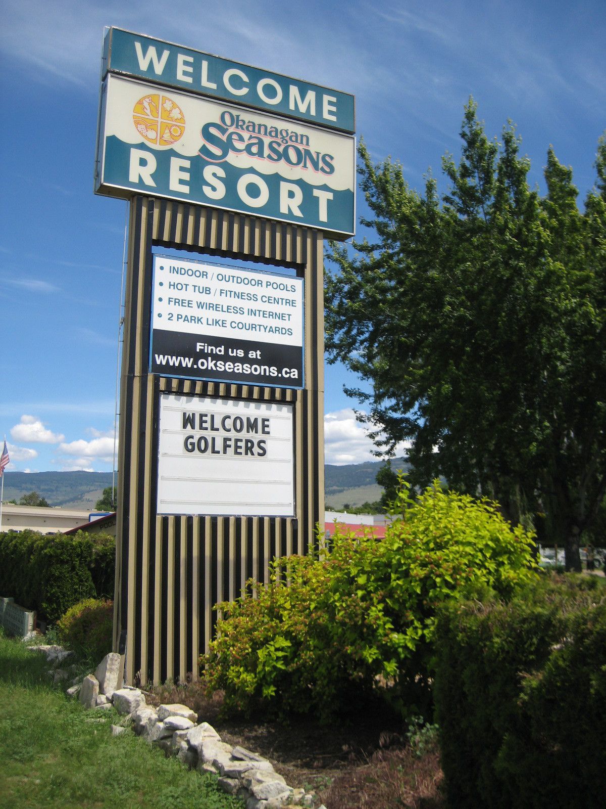 A sign for Okanagan Seasons Resort with amenities including indoor/outdoor pools, a hot tub, fitness center, free wireless internet, and 2 park-like courtyards.