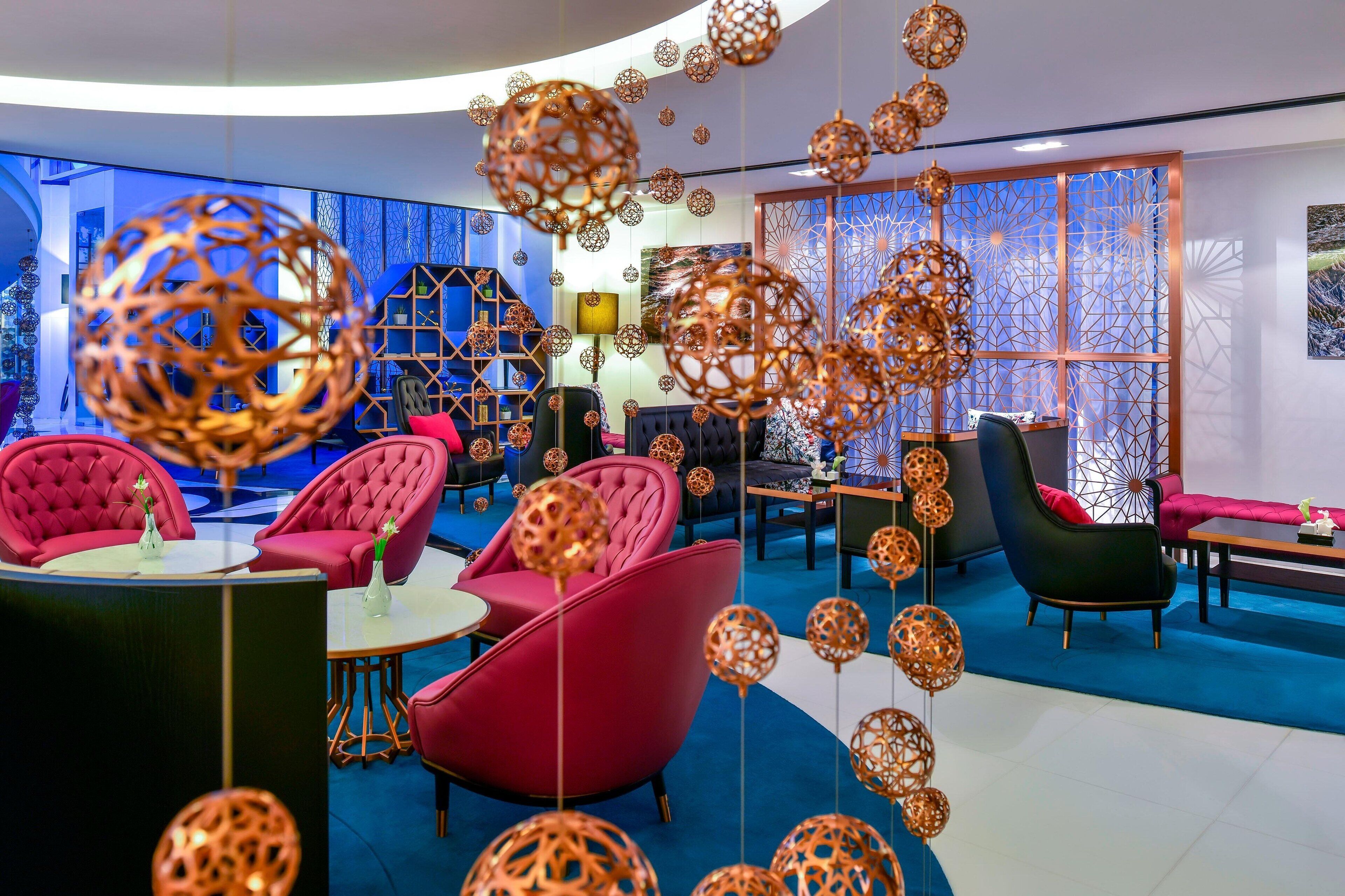 A modern lounge area with red and black upholstered chairs, a round table, and decorative hanging spheres.