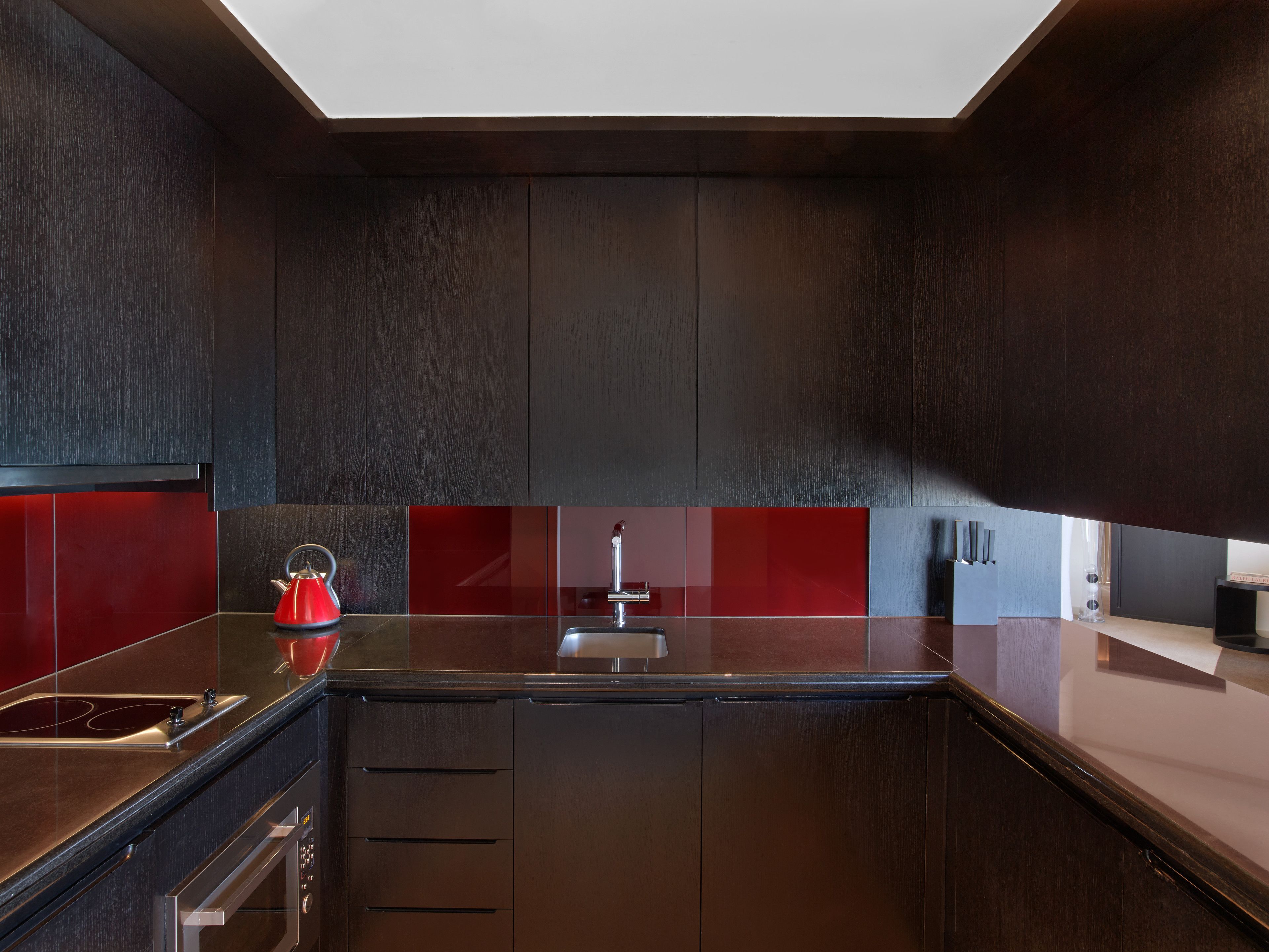 A modern kitchen with dark cabinetry, a red backsplash, and stainless steel appliances.