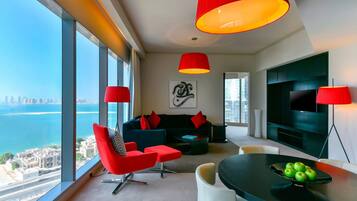 A modern living room with a large window, a black sofa, red chairs, and a dining table with green apples.