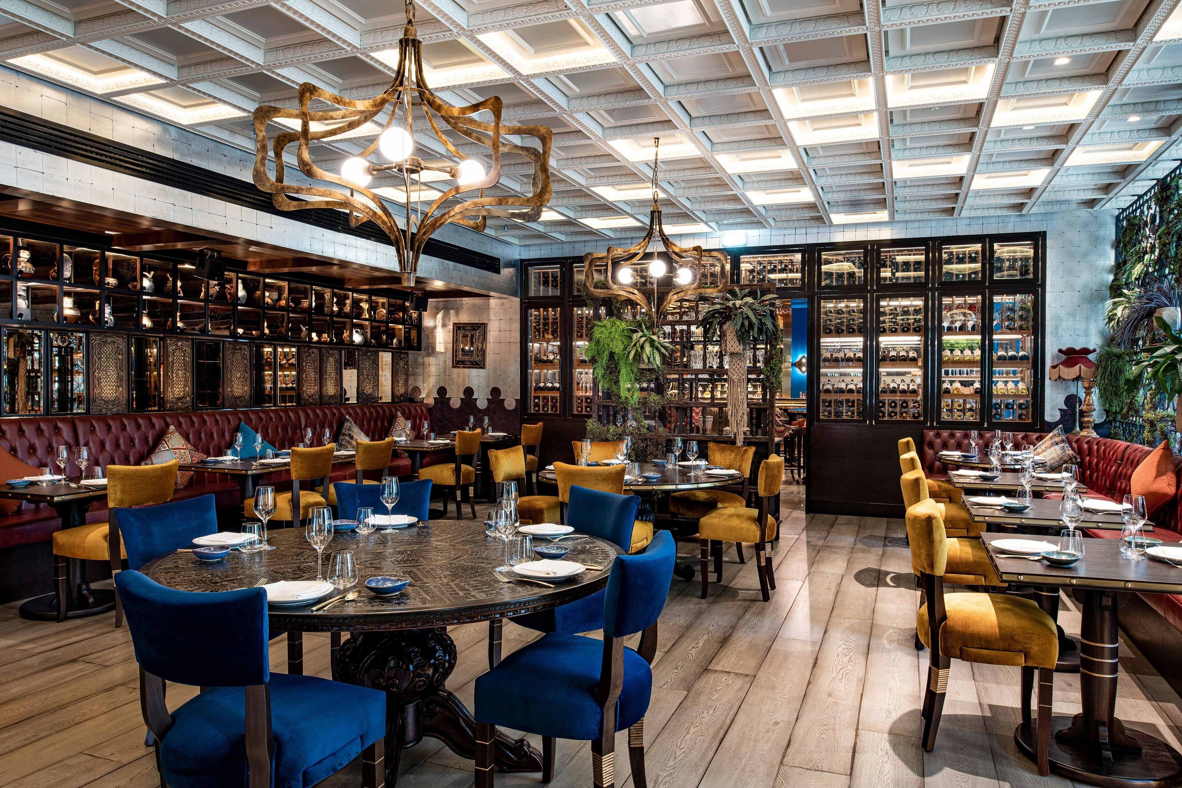 A restaurant with round tables, blue and yellow chairs, and a ceiling with a grid pattern.