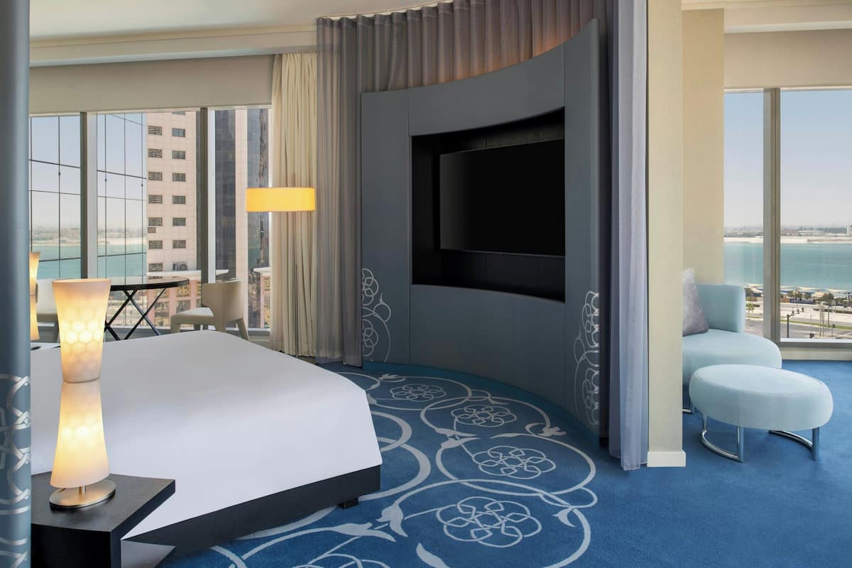 A hotel room with a bed, a TV, a desk, a chair, and a view of the city.