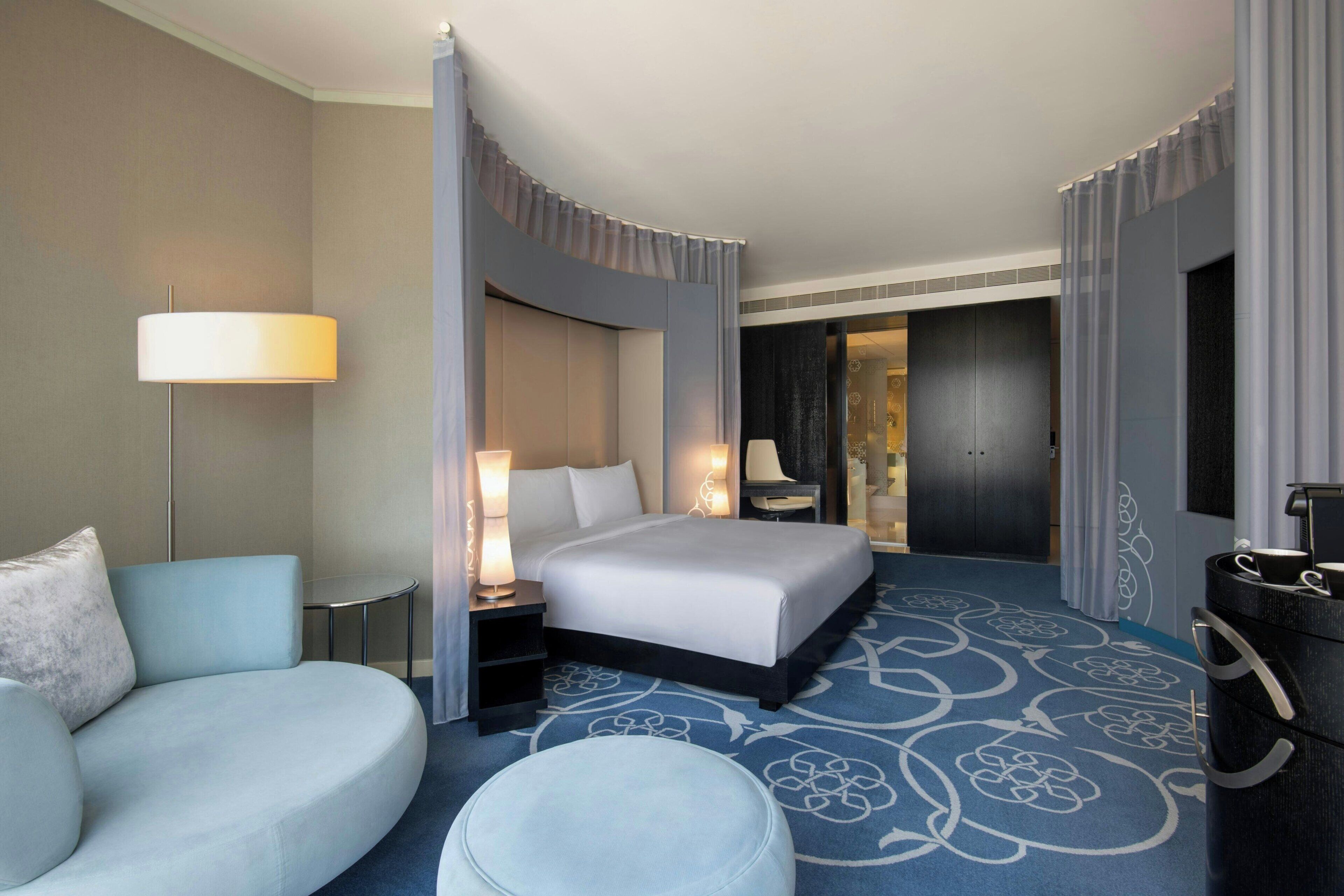 A hotel room with a bed, a sofa, a small table, a lamp, and a decorative rug.