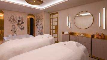 A spa room with two treatment beds, a gold-framed mirror, and a wall-mounted vanity with a sink.