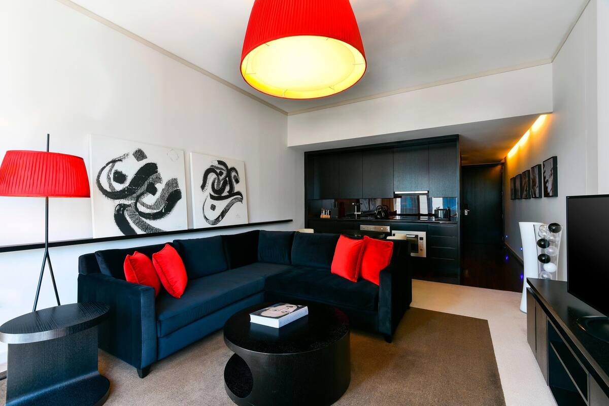 A modern living room with a dark blue sofa, red cushions, a black coffee table, and abstract wall art.