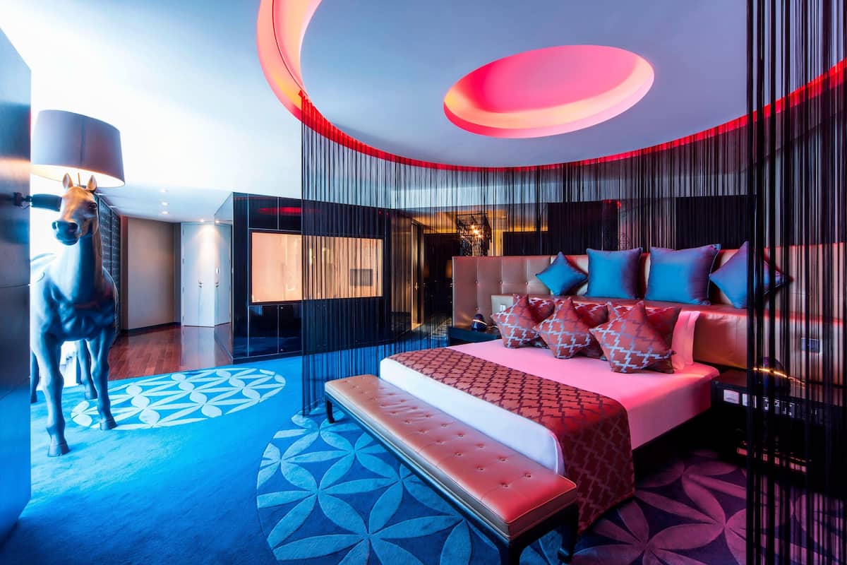 A modern bedroom with a large bed, a bench, and a decorative horse statue.