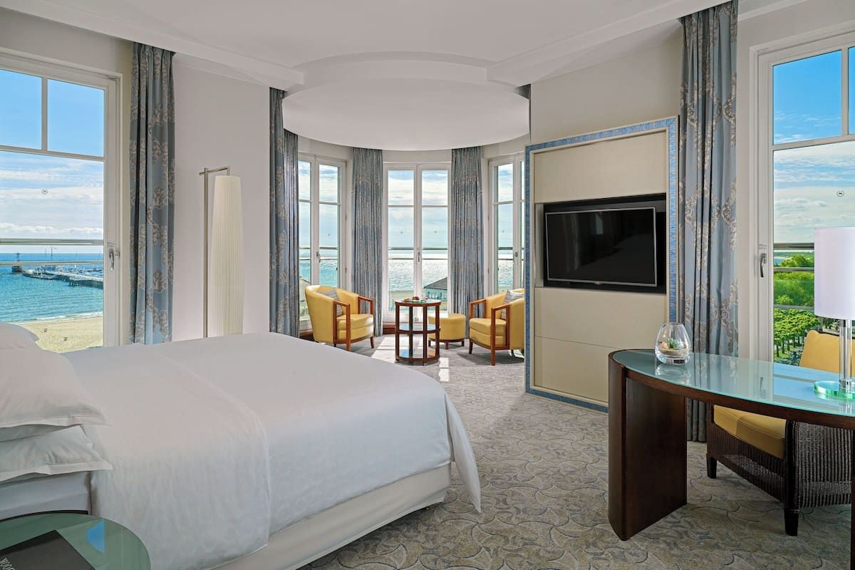 Ein Hotelzimmer mit einem großen Bett, einem Fernseher, einem Schreibtisch und Blick auf das Meer.