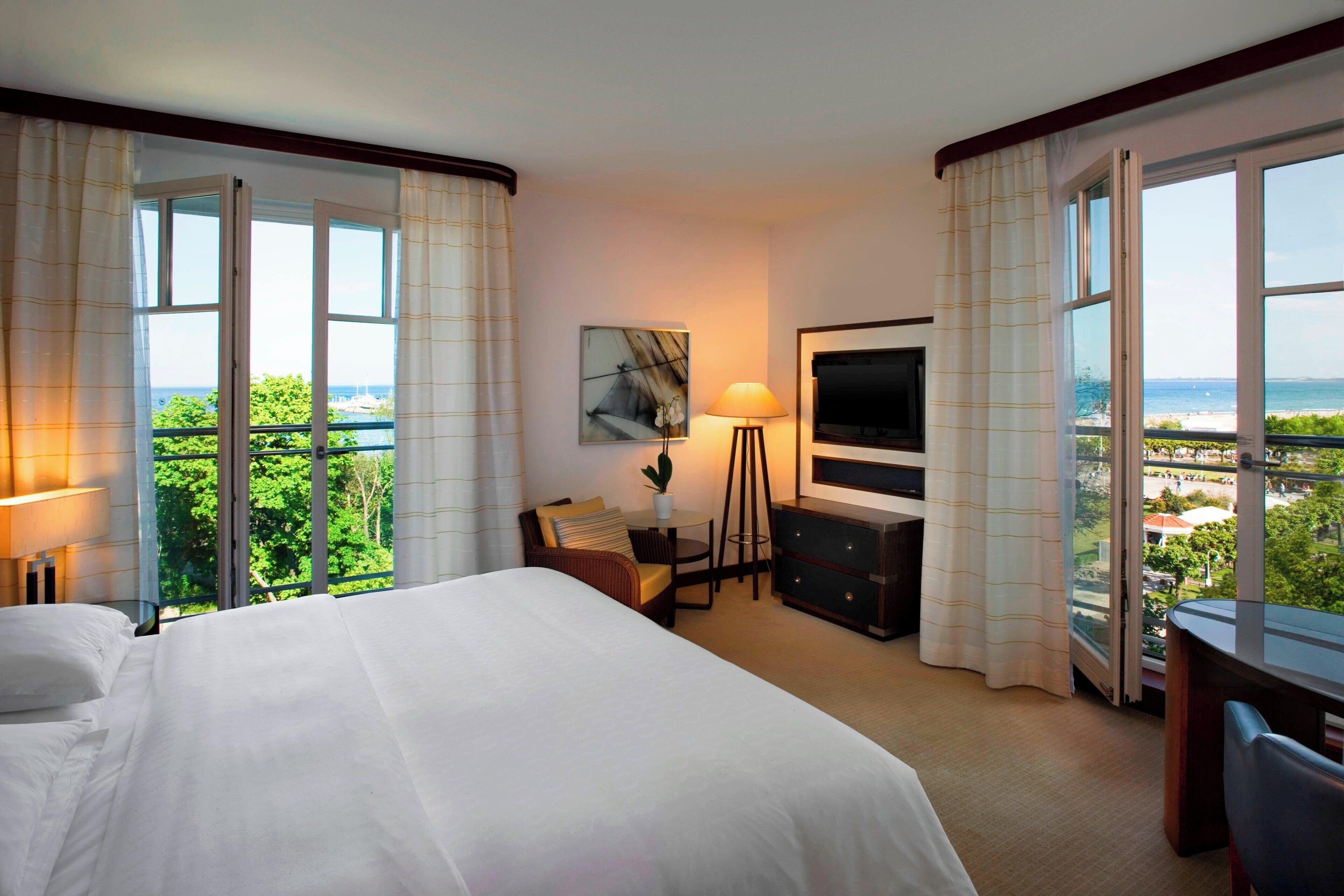 Habitación de hotel con cama, escritorio, silla, televisor y vista al mar.
