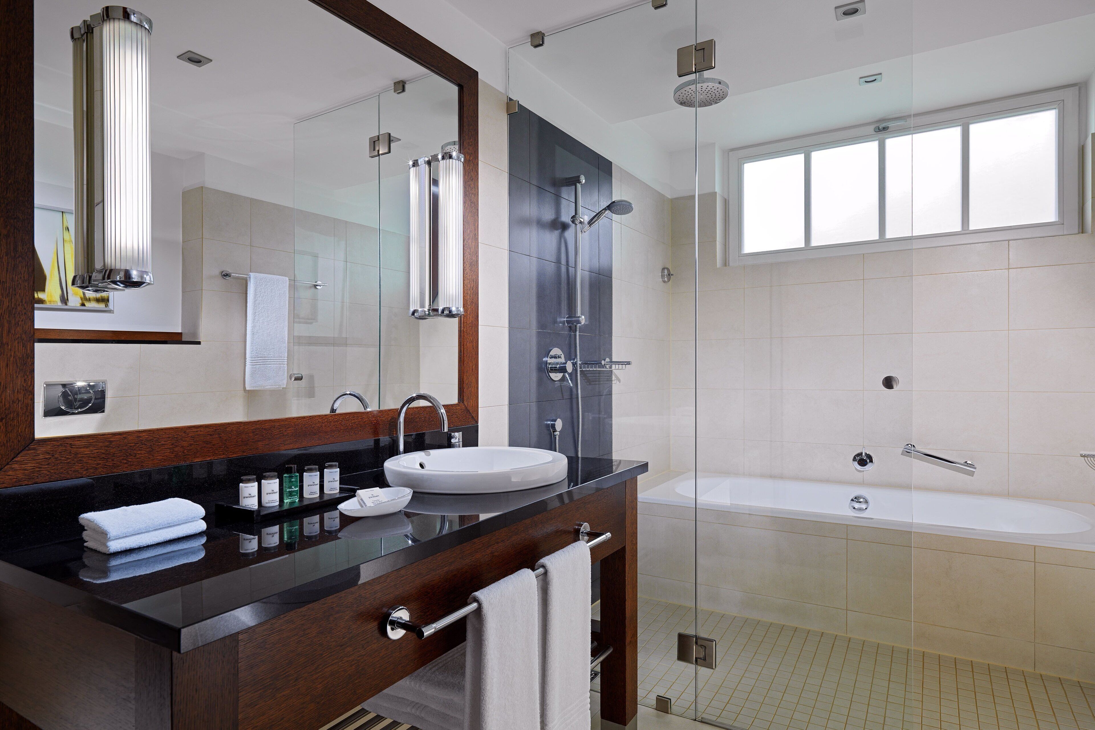 Un baño moderno con ducha envuelta en vidrio, un espejo grande, tocador con lavamanos y bañera.