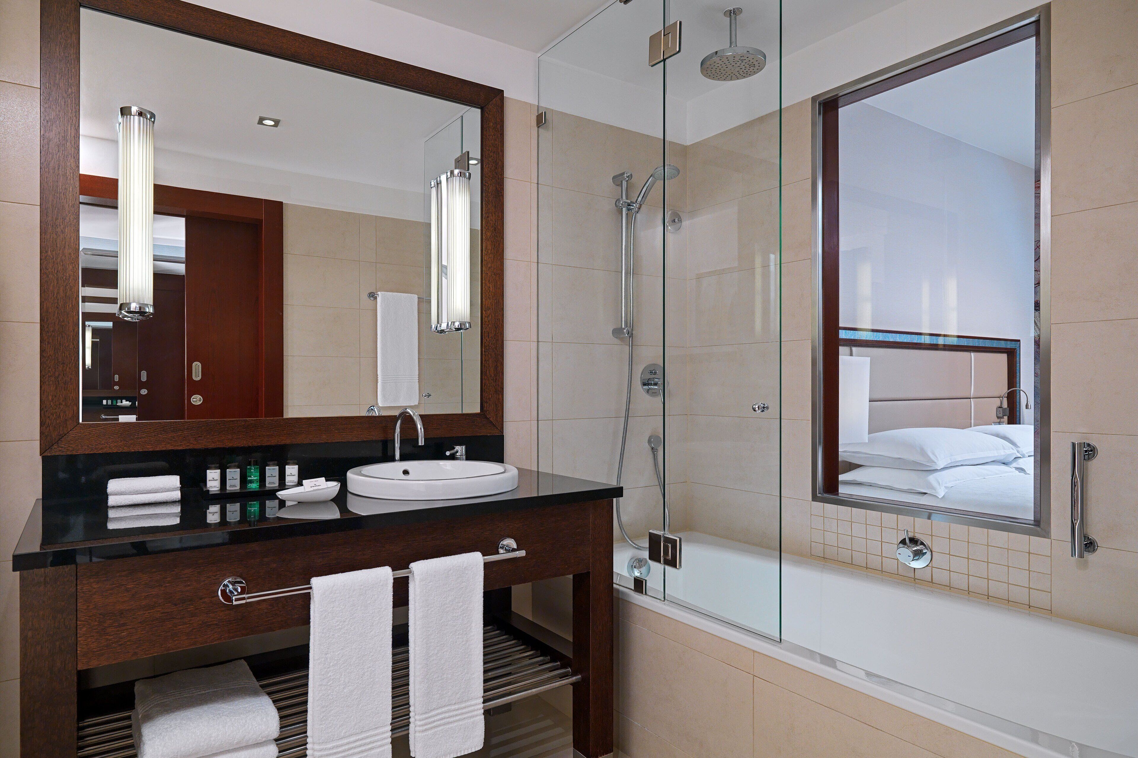 A modern bathroom with a glass-enclosed shower, a large mirror, a dark wooden vanity, and a white sink.