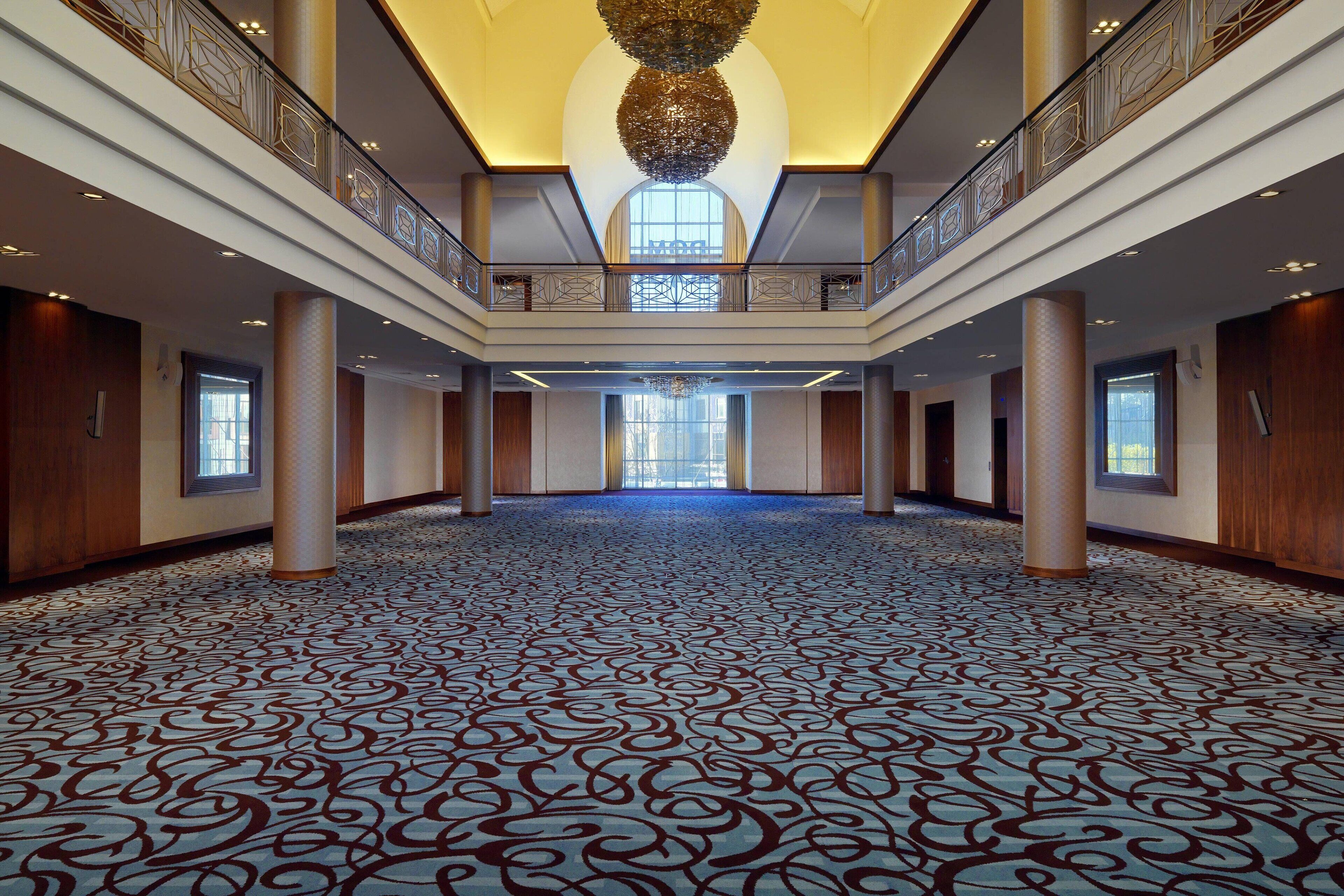 A spacious hall with a patterned carpet, high ceilings, and a central chandelier.