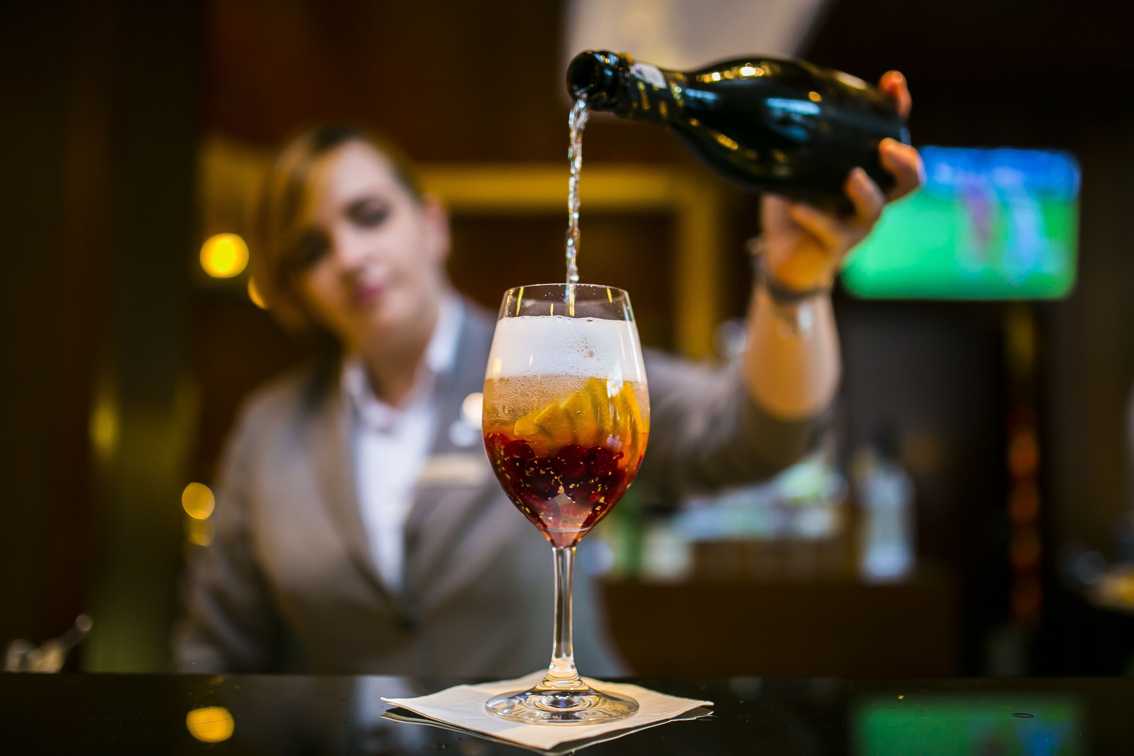 Un barman verse une boisson dans un verre décoré de fruits.