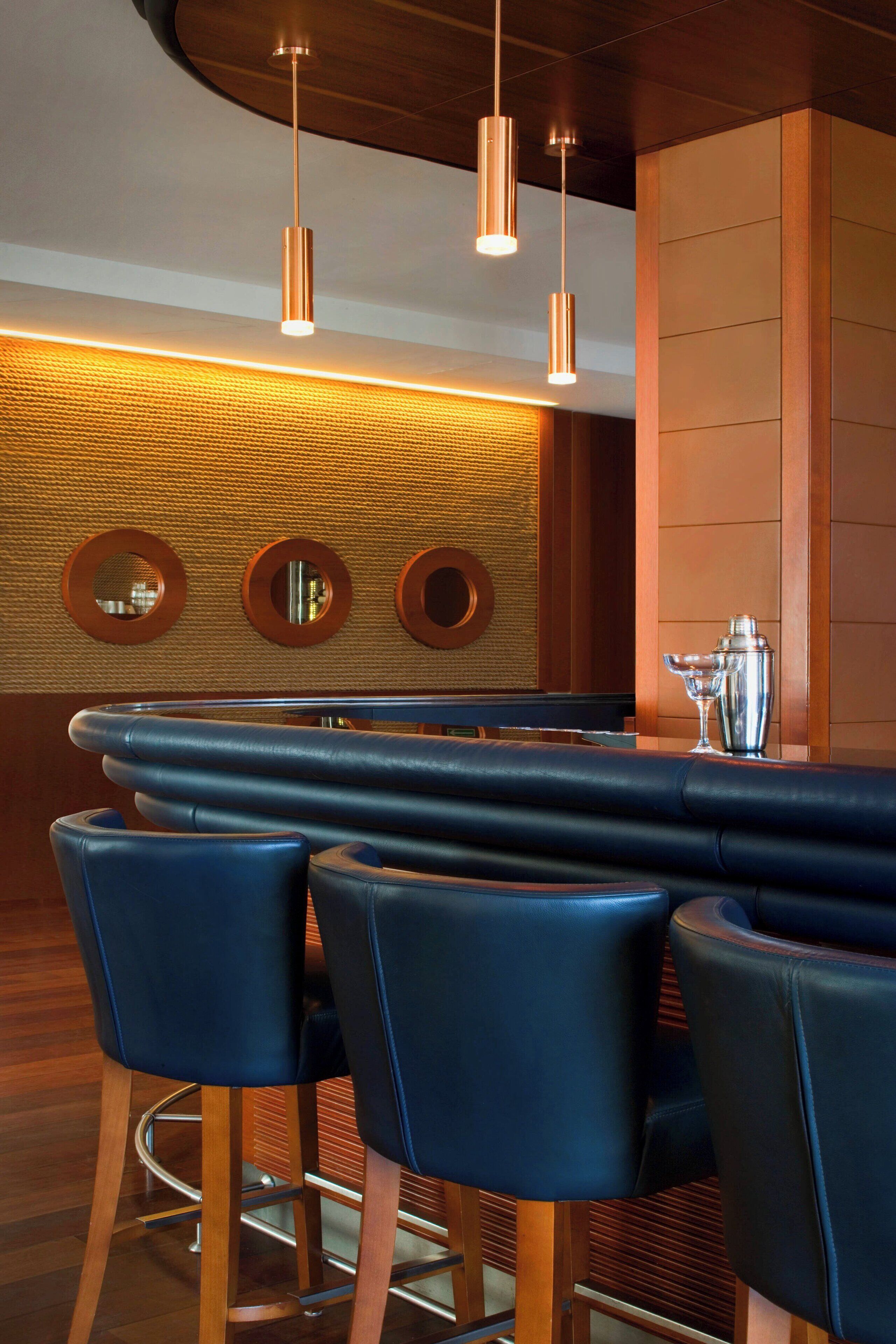 A bar area with a long counter, three high bar stools, and pendant lighting.