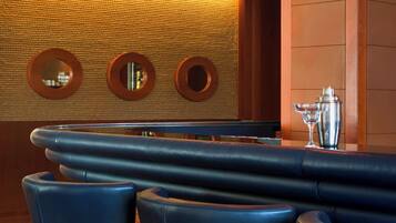 A bar area with a long counter, three high bar stools, and pendant lighting.