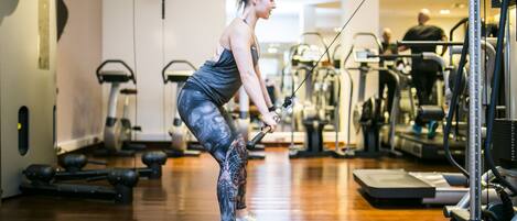 A gym with exercise equipment, wooden flooring, and a person using a cable machine.