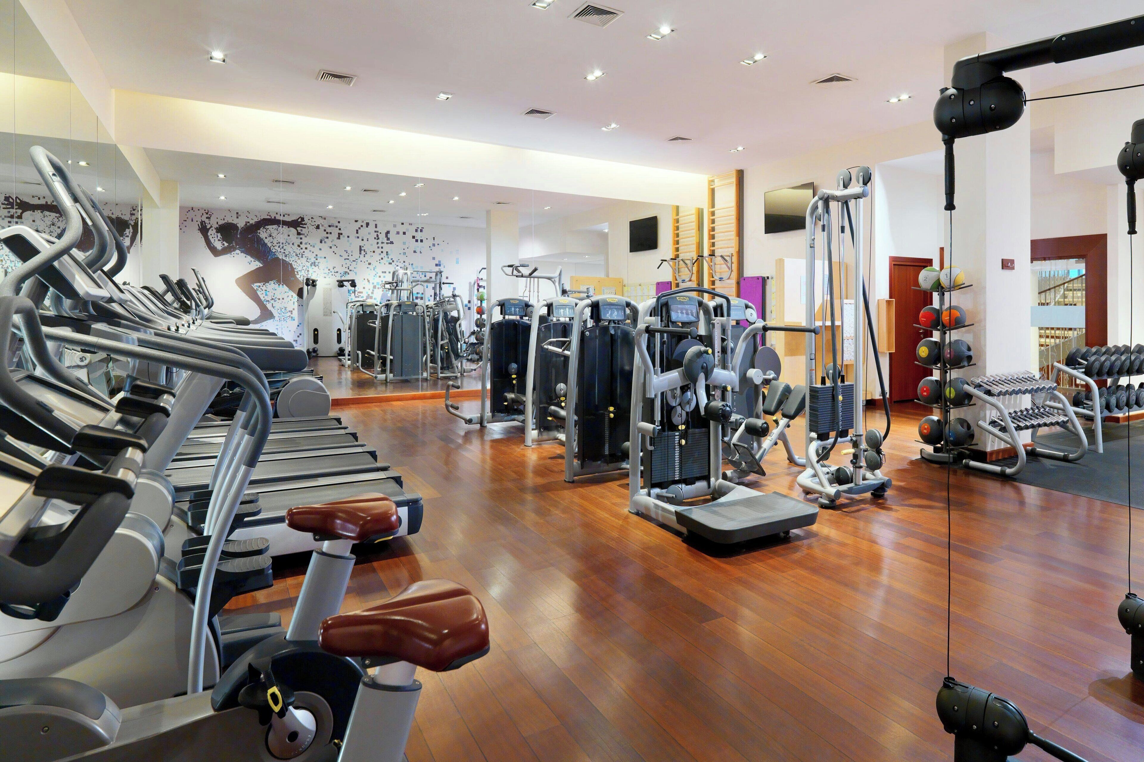 Een fitnessruimte met loopbanden, krachttrainingsapparaten en een spiegelwand.