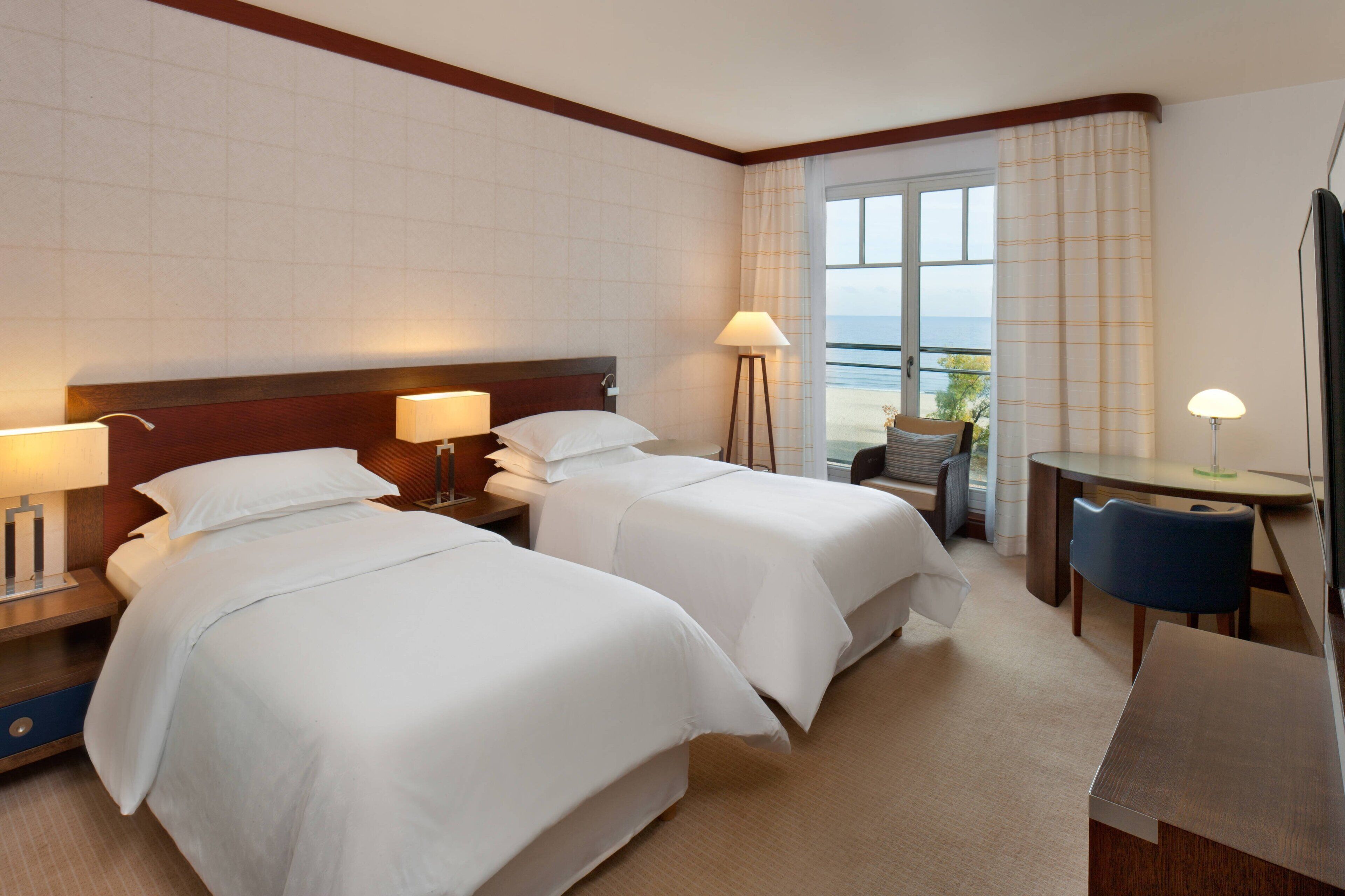 Habitación de hotel con dos camas, un escritorio, una silla y vista al mar.