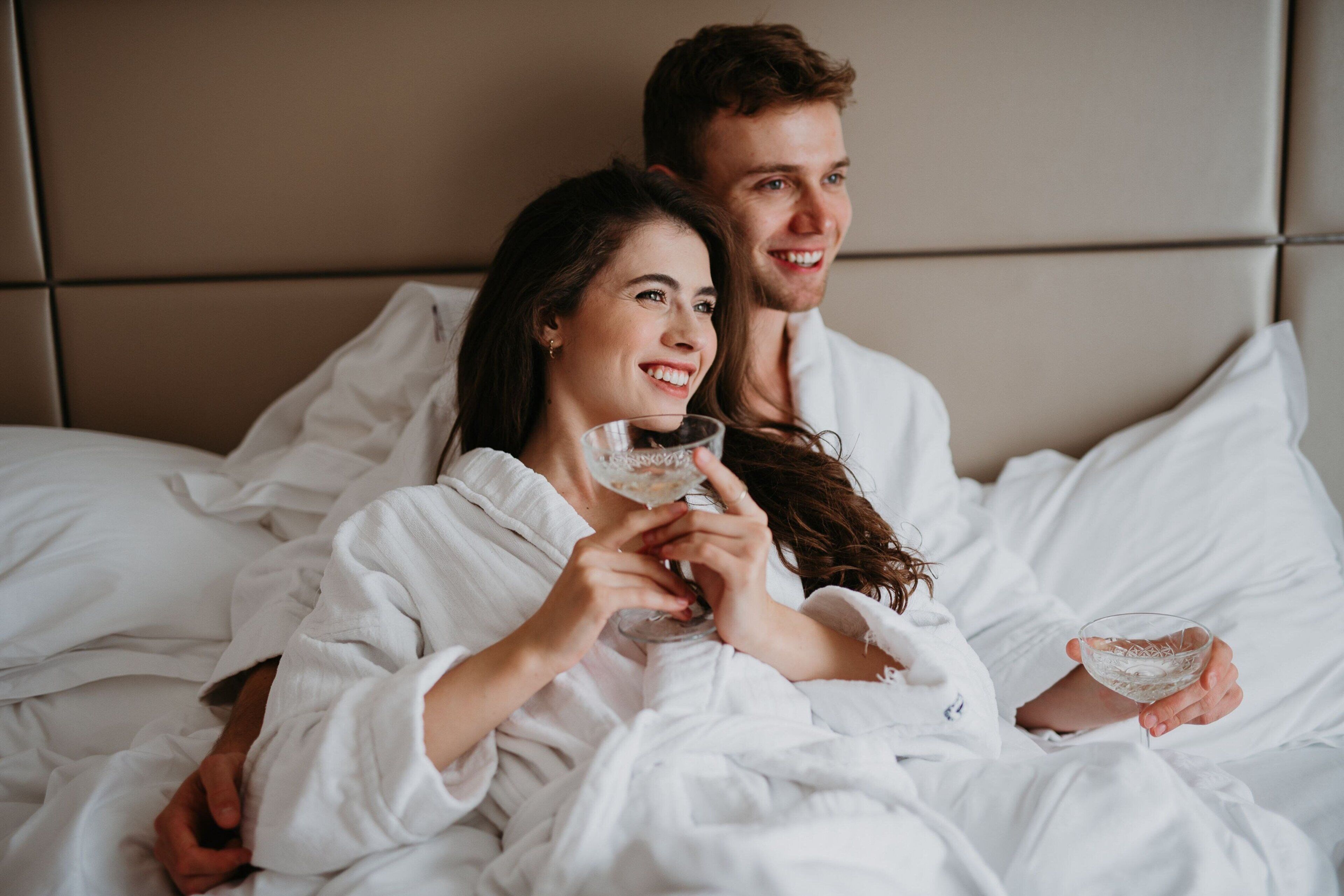 Una pareja en un dormitorio con cama, almohadas y cabecero.