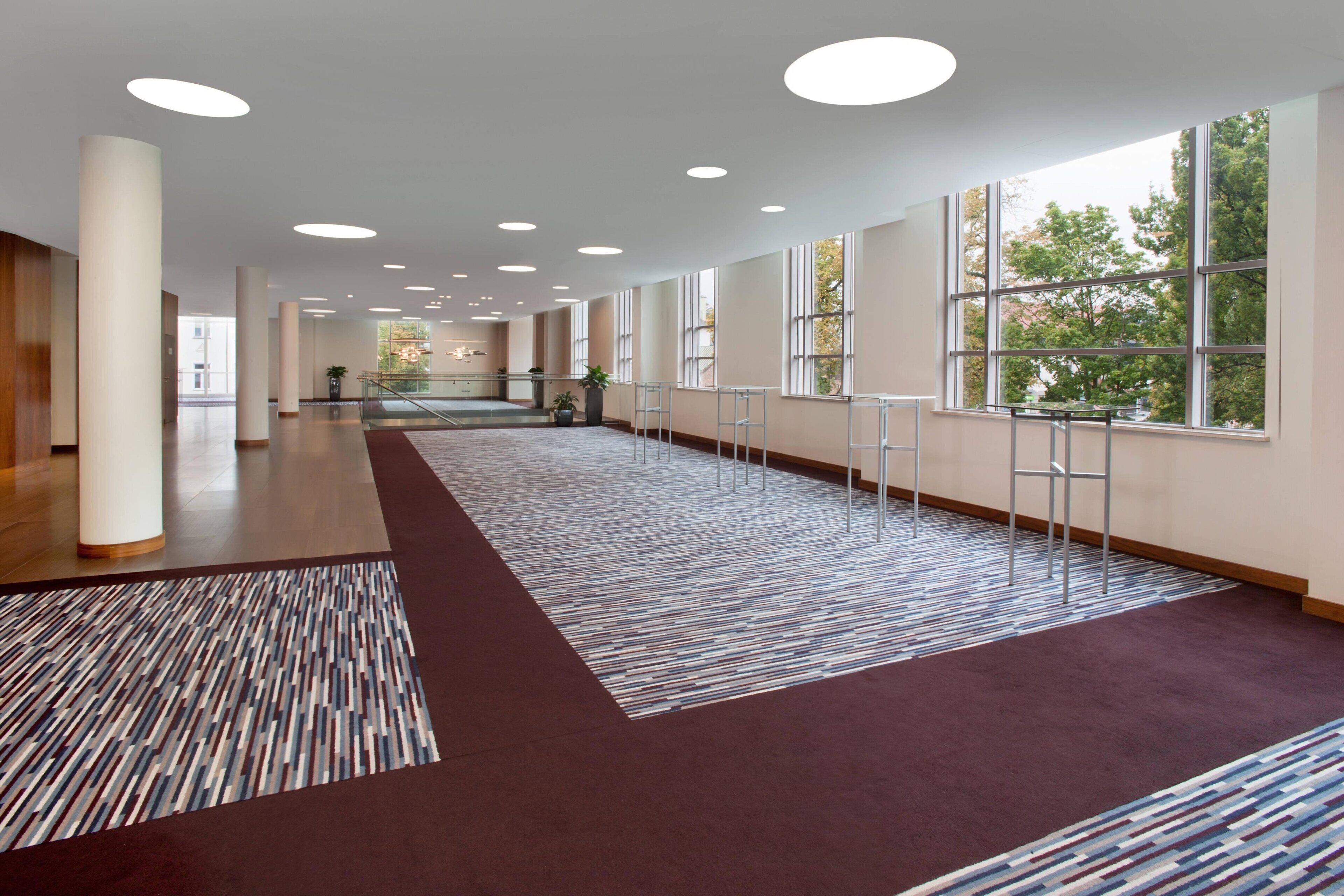 A spacious corridor with a patterned carpet, large windows, and a modern ceiling design.