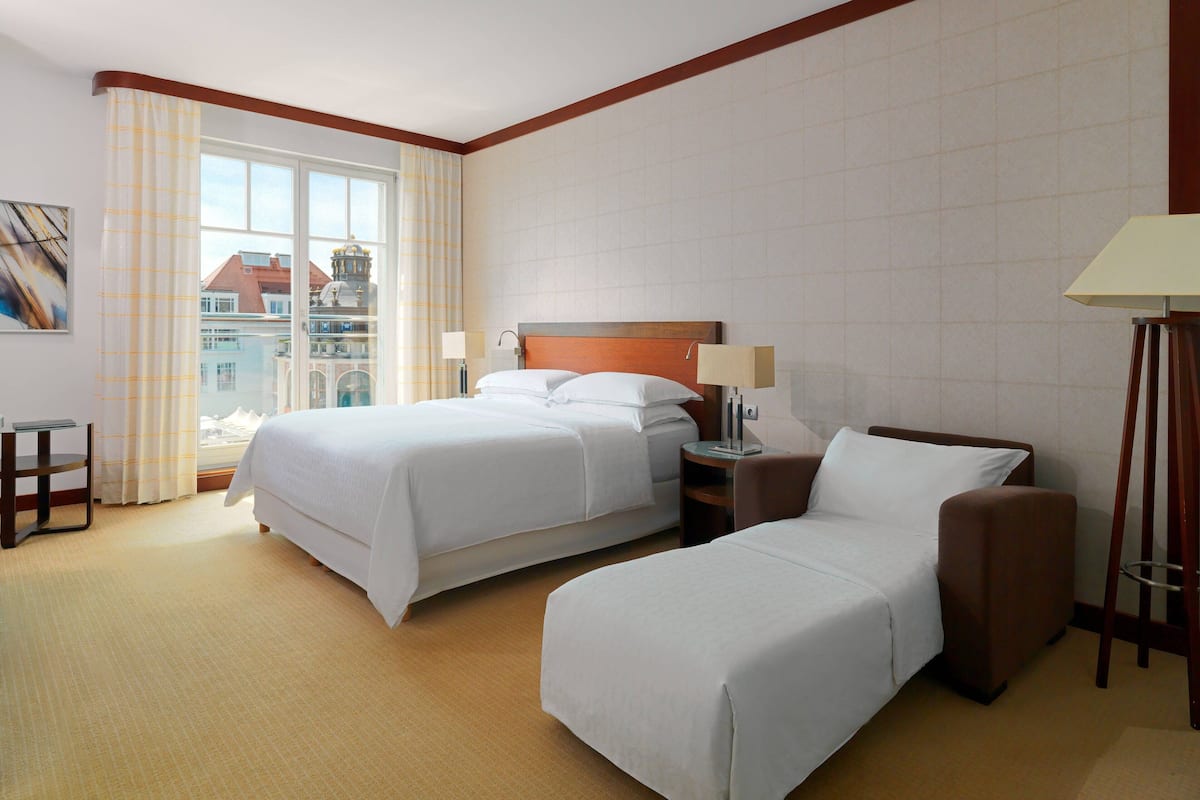 Ein Hotelzimmer mit zwei Betten, einem Schlafsofa, einem Schreibtisch und einer Lampe.