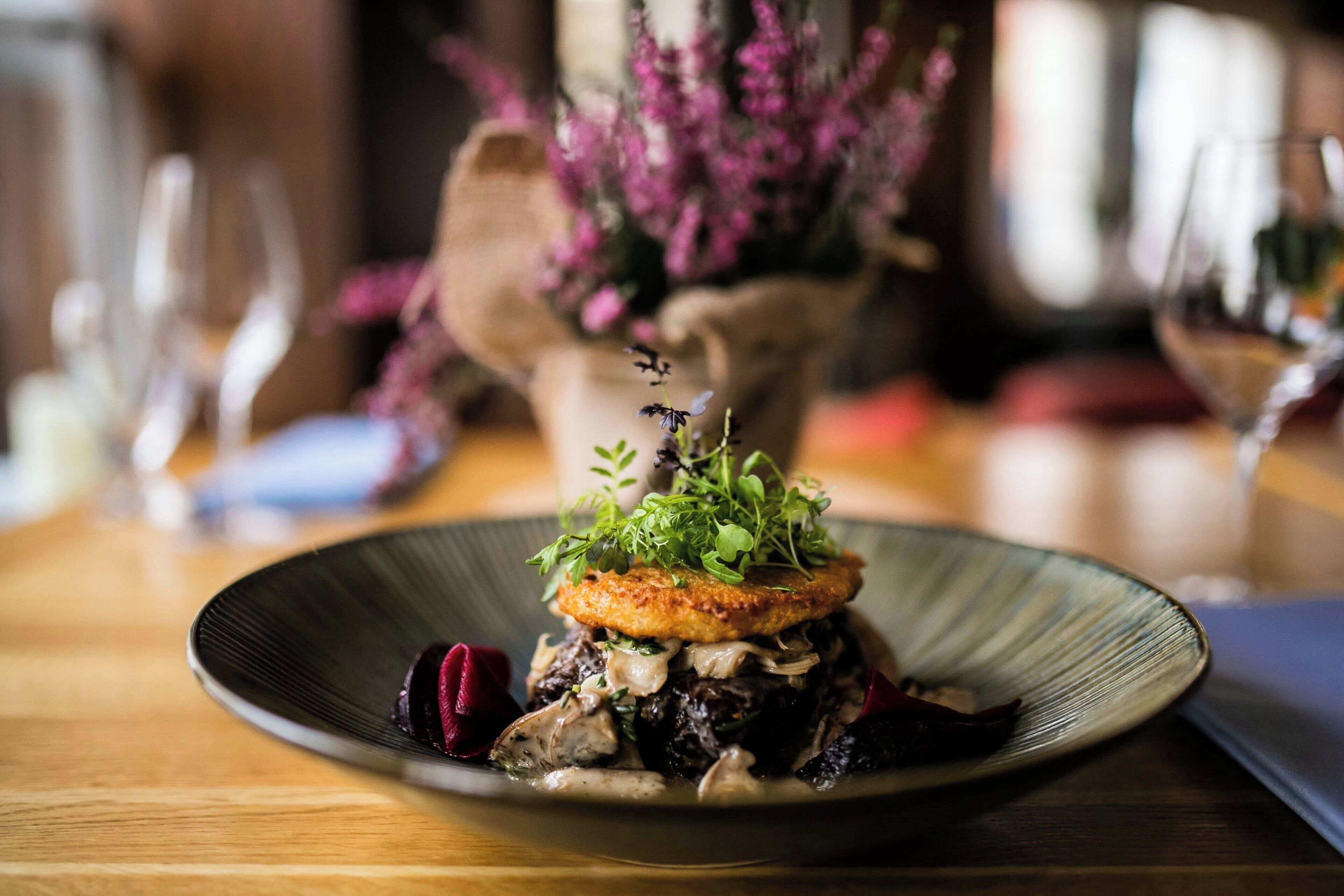 A plate of food with a variety of ingredients, including greens and mushrooms, on a dark plate.
