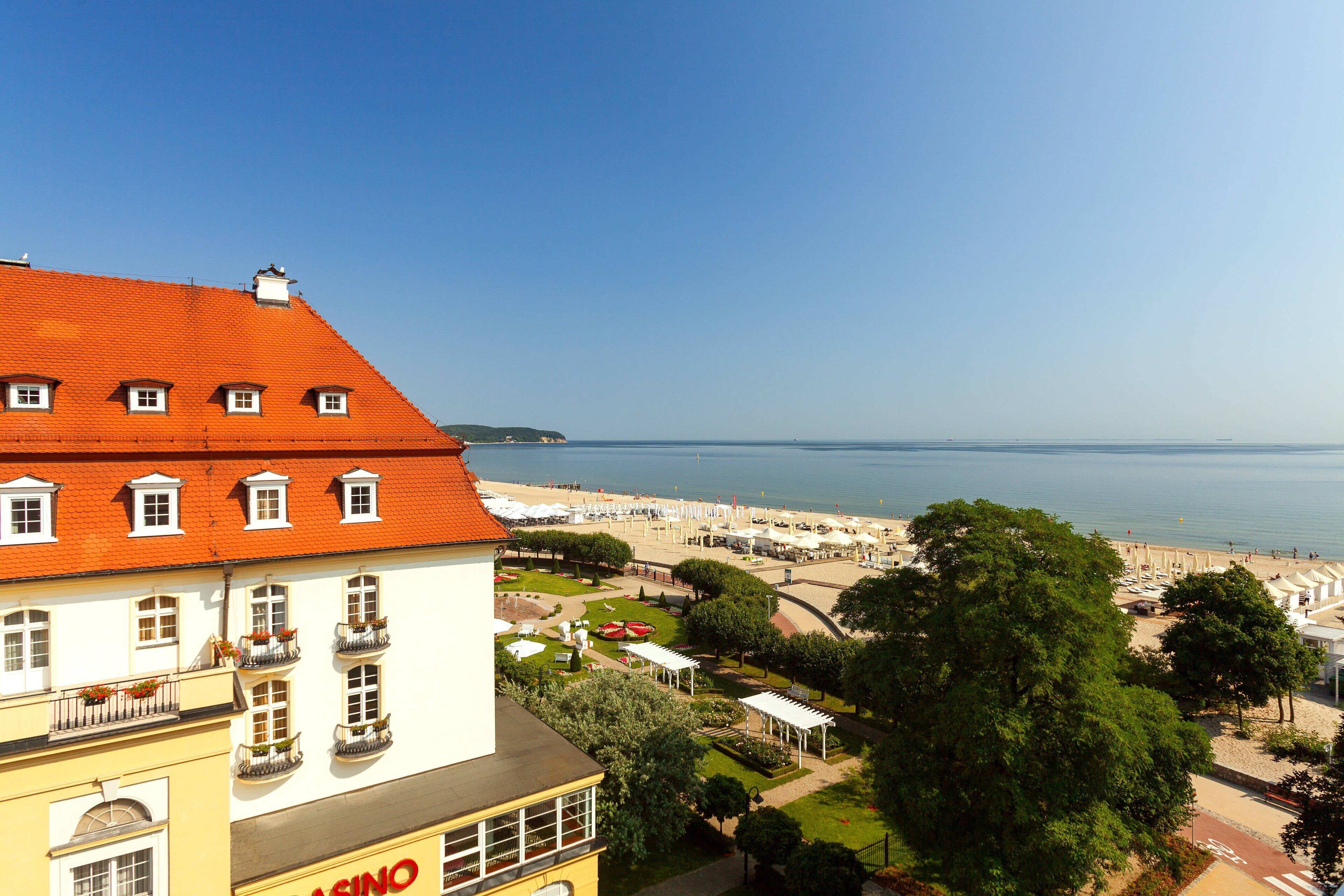 Een kusthotel met een rood pannendak, een zichtbaar casino bord en uitzicht op het strand.