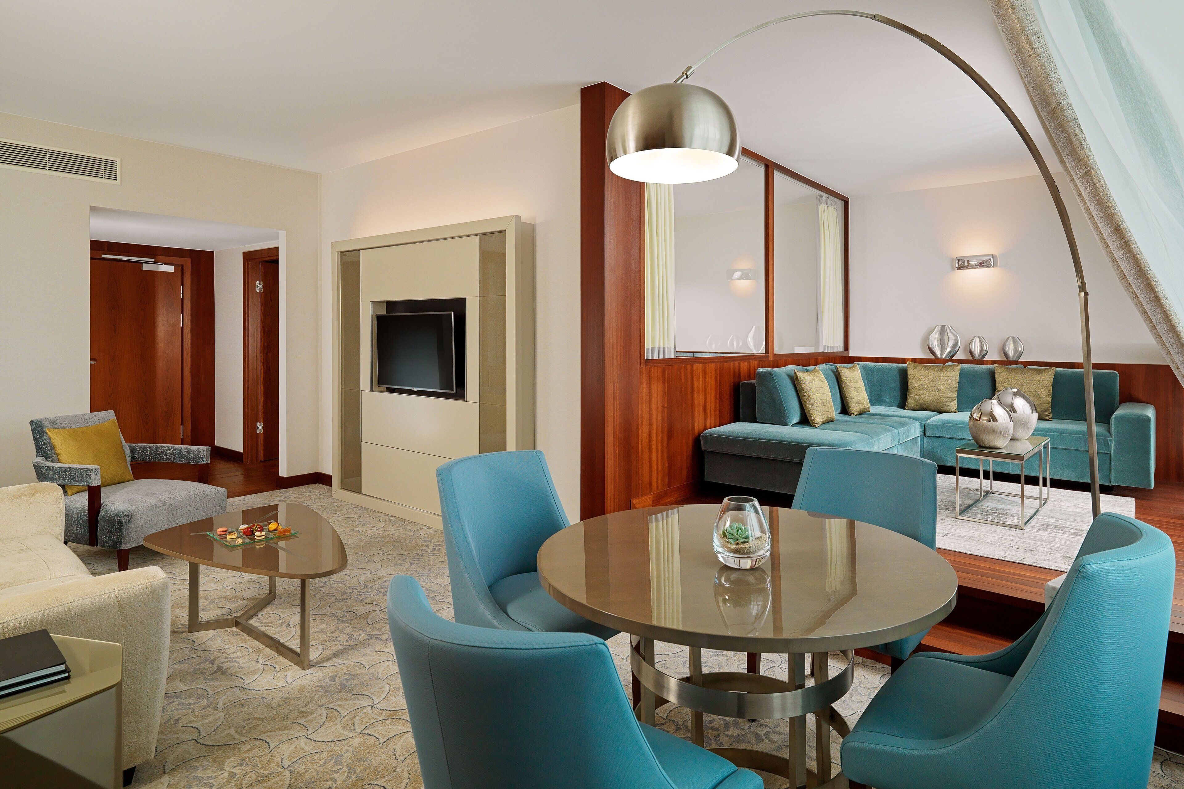 A modern hotel room with a sofa, armchairs, a coffee table, and a TV.