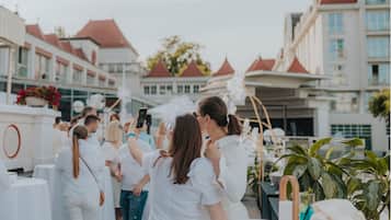 Un grupo de personas vestidas de blanco en un evento al aire libre, con un edificio de fondo que tiene techos rojos y paredes blancas.