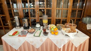 Una mesa de desayuno buffet con diversas opciones de comida y bebidas, con grandes ventanales de madera al fondo.