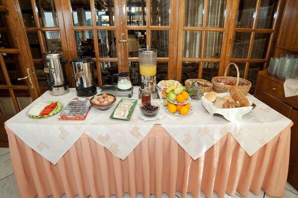 Una mesa de desayuno buffet con diversas opciones de comida y bebidas, con grandes ventanales de madera al fondo.