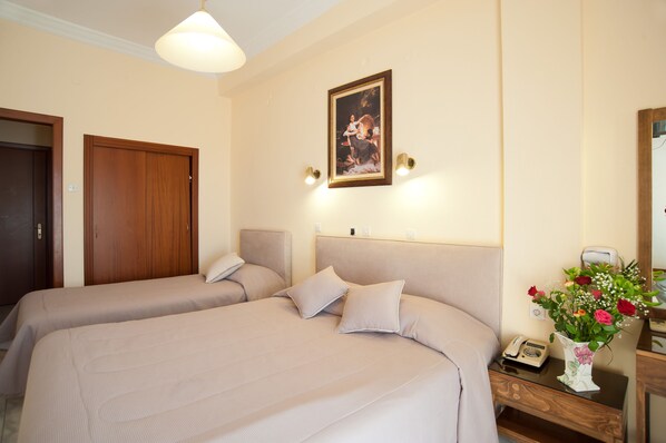 Habitación de hotel con dos camas, una puerta de madera, un cuadro enmarcado en la pared, una mesita de noche con un teléfono y un jarrón de flores.
