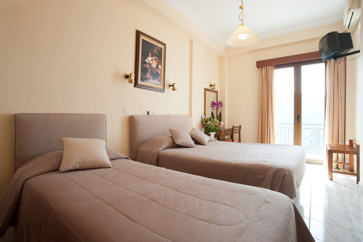 Une chambre d’hôtel avec deux lits, un balcon et une télévision.