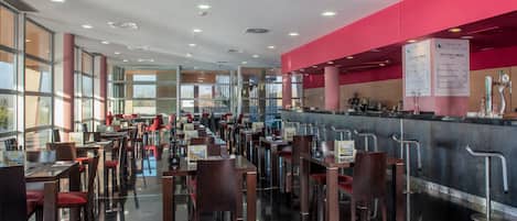 A spacious restaurant with multiple tables and chairs, a counter with a menu, and large windows allowing natural light.