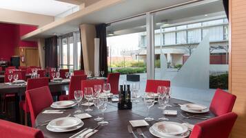 Comedor con mesas dispuestas para cuatro, sillas rojas y vistas del edificio.