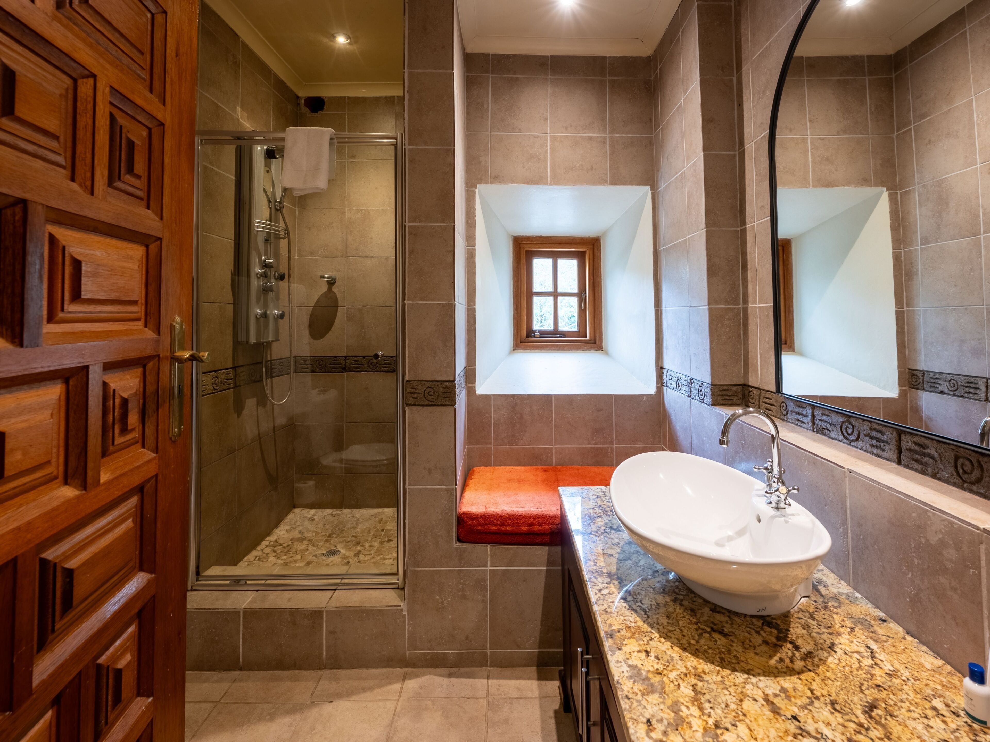 A bathroom with a glass-enclosed shower, a sink with a granite countertop, and a mirror with a decorative frame.