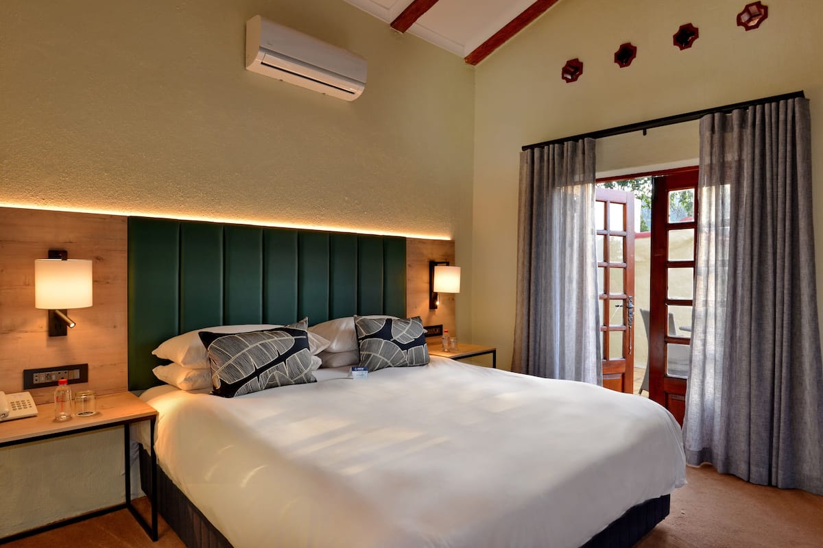 A hotel room with a large bed, two bedside lamps, an air conditioner, and a view through a door.