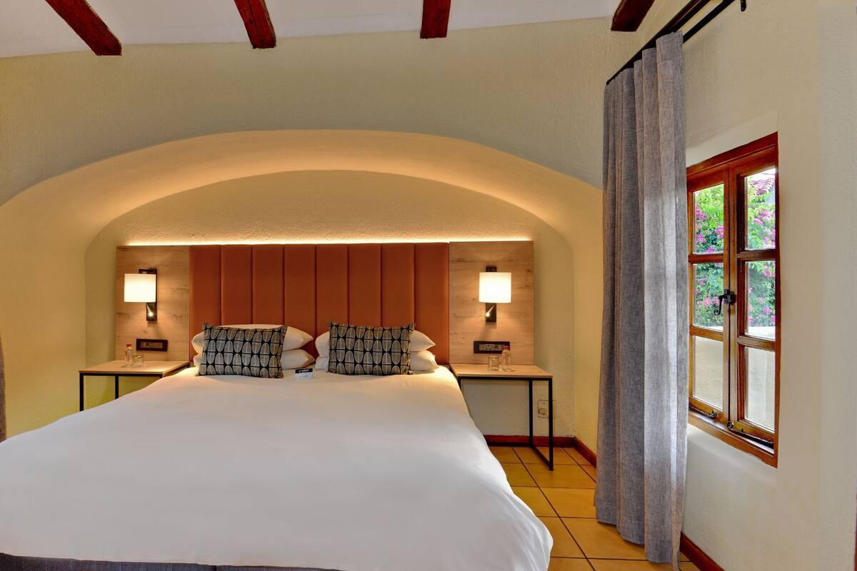 A hotel room with a large bed, two bedside tables with lamps, and a window with curtains.