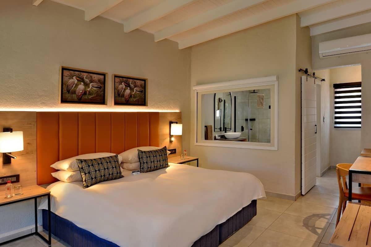 A hotel room with a large bed, bedside lamps, a desk with a chair, a television, and artwork on the wall.