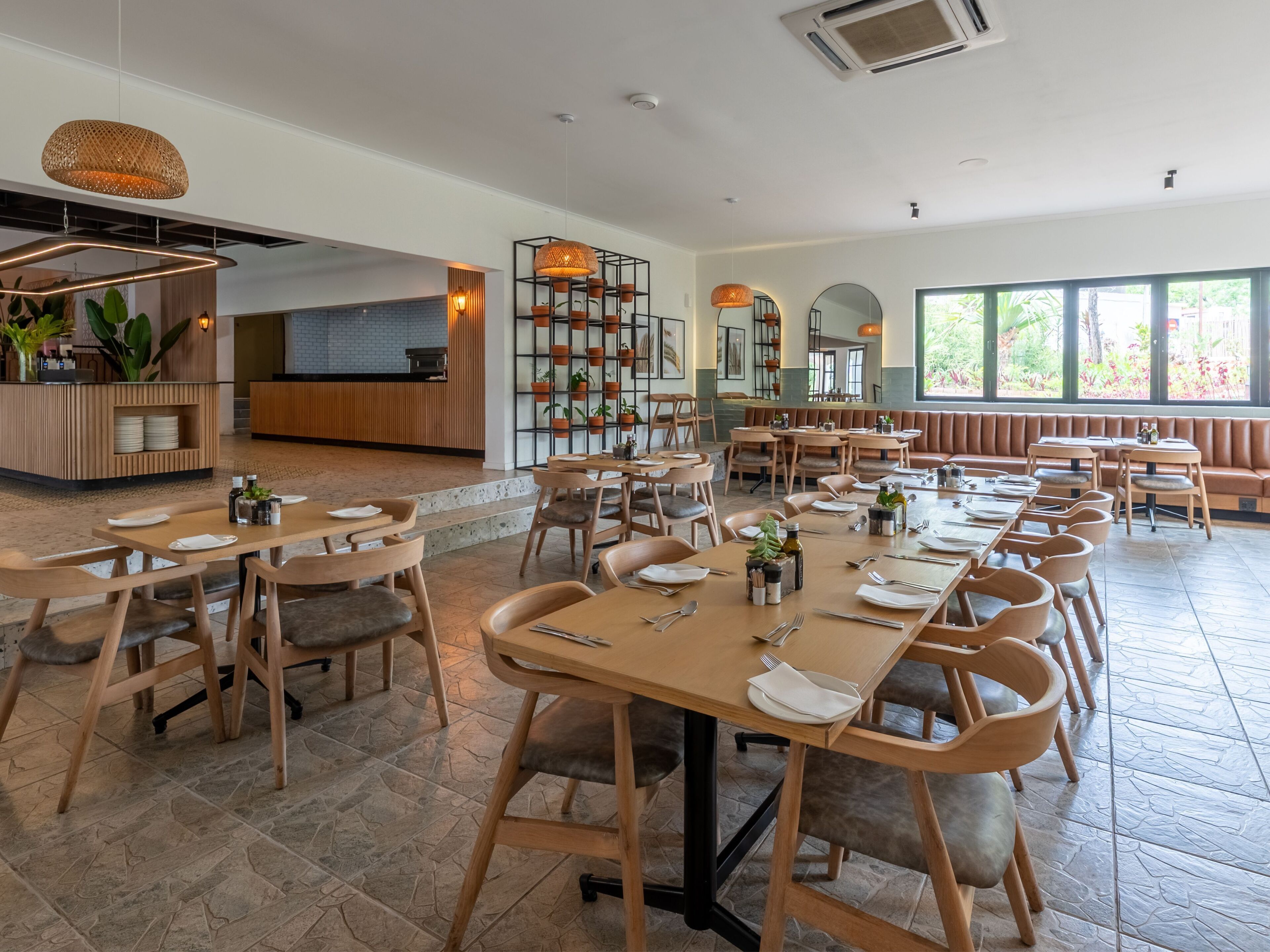 Un comedor amplio con varias mesas y sillas, una cocina al fondo y ventanas grandes que dejan entrar luz natural.