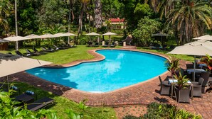 A swimming pool with lounge chairs and umbrellas, surrounded by lush greenery and palm trees.