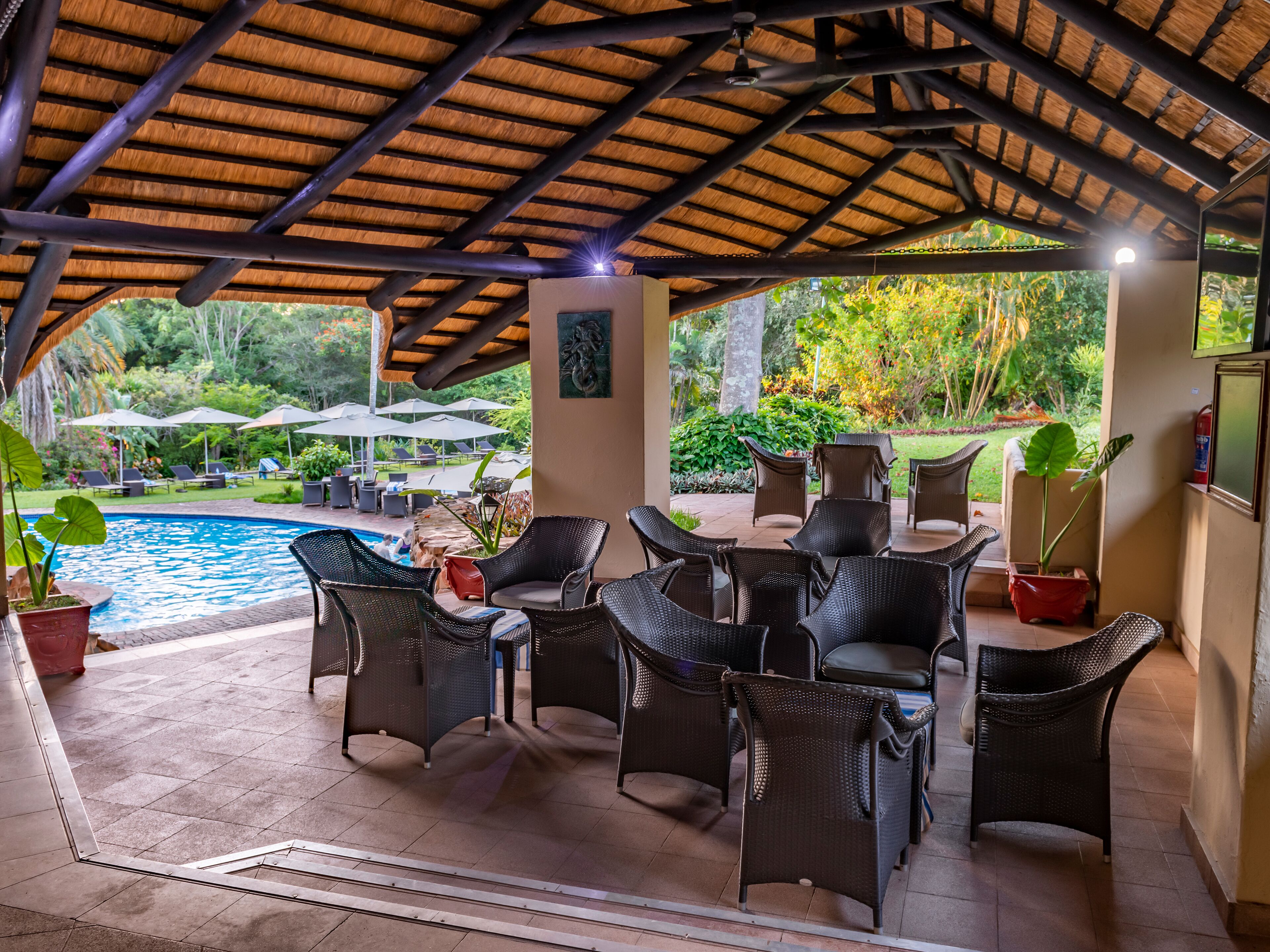 Un patio exterior con mobiliario de mimbre, una piscina y sombrillas.