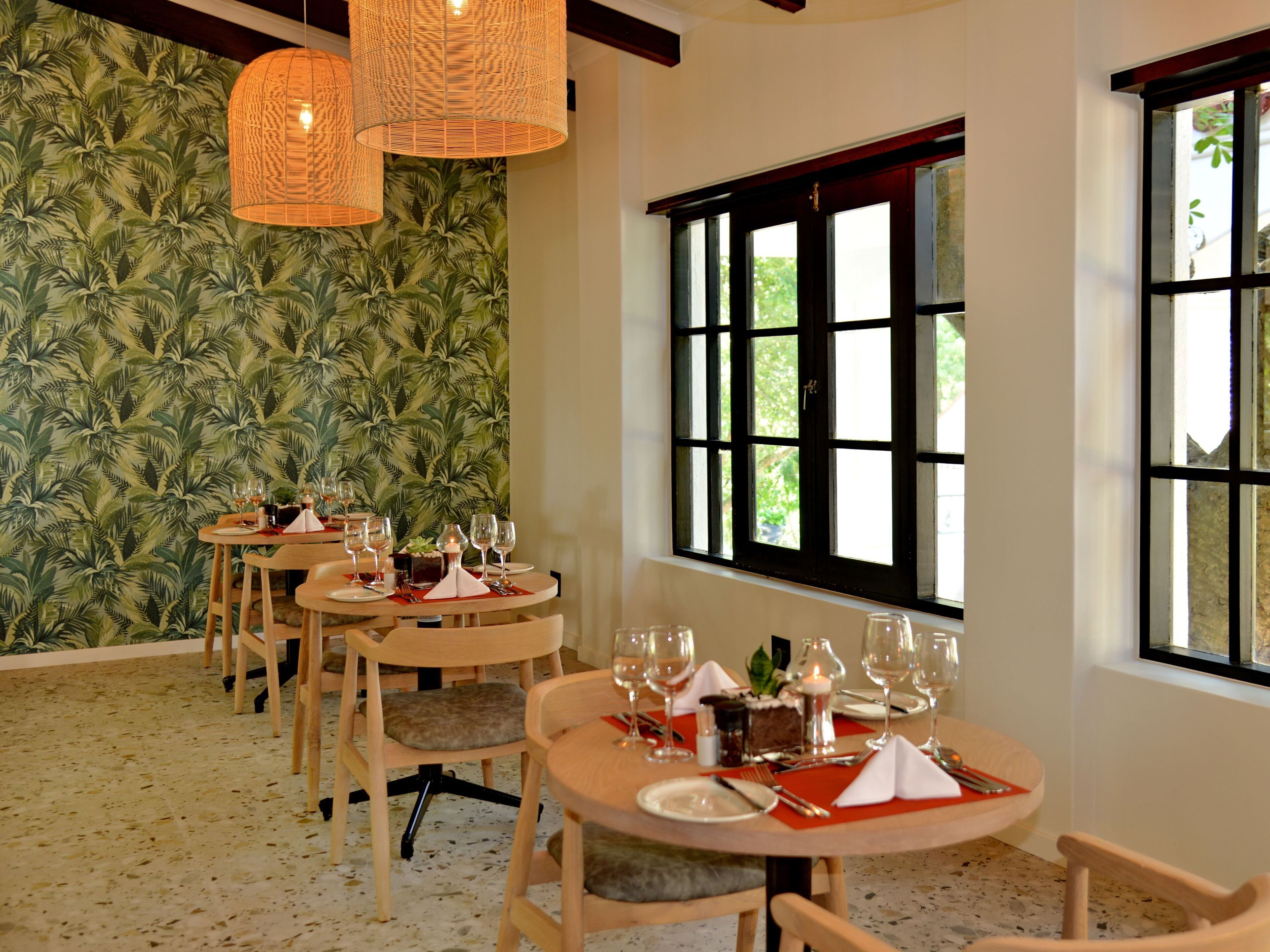 A dining area with round tables, chairs, and a tropical wallpaper.
