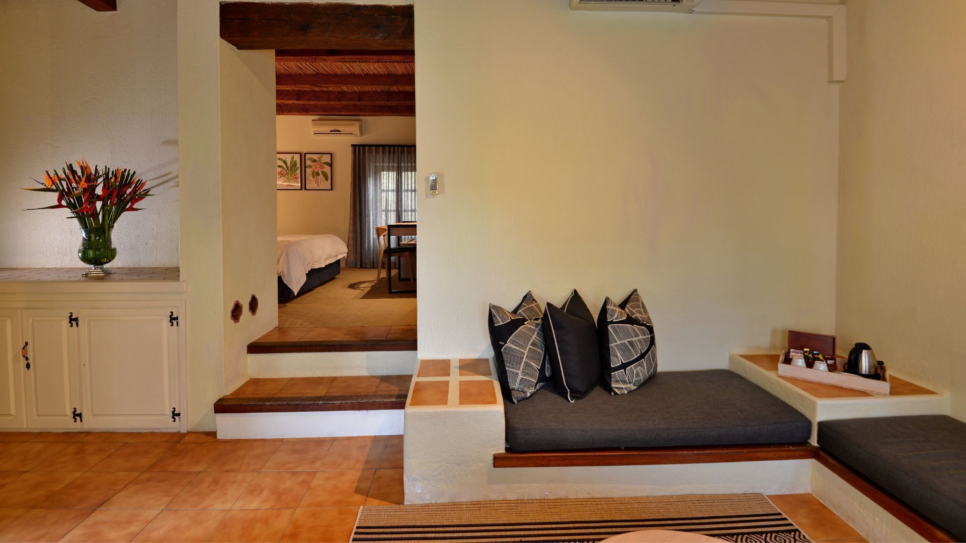 A cozy room with a sofa, pillows, a small table with a kettle, and a vase with flowers.