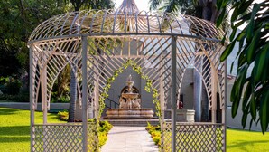 A gazebo with a fountain, surrounded by a garden and a pathway.